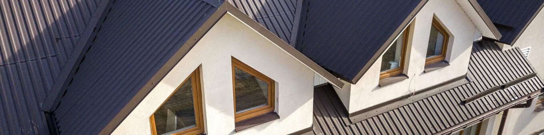 Close Up Aerial View Of Building Attic Rooms Exterior On Metal Shingle Roof, Stucco Walls And Plastic Windows.